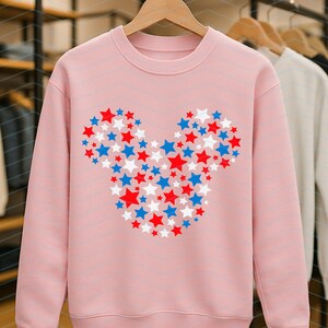 May include: A light pink crewneck sweatshirt featuring a central graphic composed of numerous small red, white, and blue stars arranged to form the distinct silhouette of a mouse head with two circular ears and a rounded face shape.