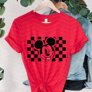 May include: Red t-shirt with a black and white checkered design featuring a cartoon Mickey Mouse with a wink.