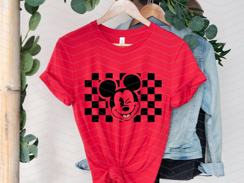 May include: Red t-shirt with a black and white checkered design featuring a cartoon Mickey Mouse with a wink.