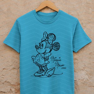 May include: A turquoise t-shirt with a sketch of Minnie Mouse in black ink. The design includes Minnie's signature bow, dress, and shoes. The words "Minnie Mouse xoxo" are written in cursive below the character.