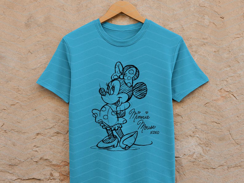 May include: A turquoise t-shirt with a sketch of Minnie Mouse in black ink. The design includes Minnie's signature bow, dress, and shoes. The words "Minnie Mouse xoxo" are written in cursive below the character.