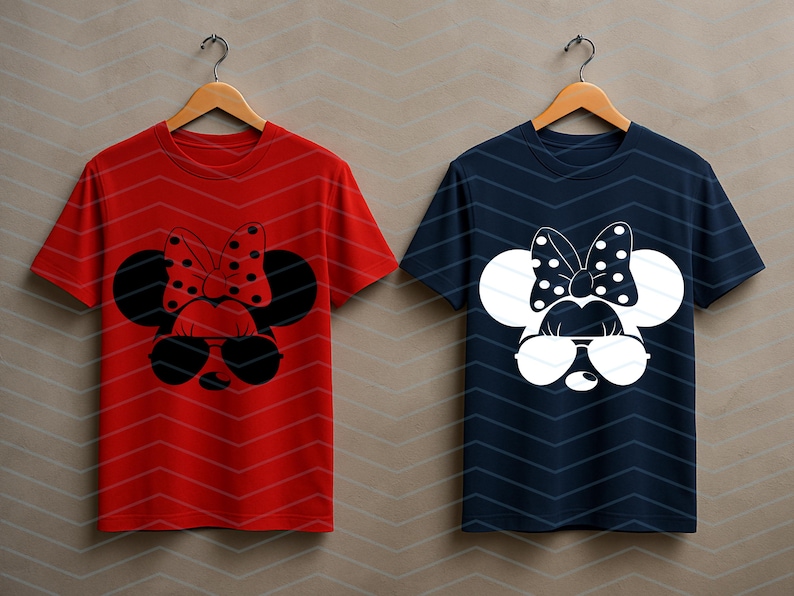 May include: Two t-shirts hanging on wooden hangers. One is red with a black and red polka-dot bow and sunglasses design. The other is navy blue with a white polka-dot bow and sunglasses design. Both shirts have a Minnie Mouse-inspired graphic.
