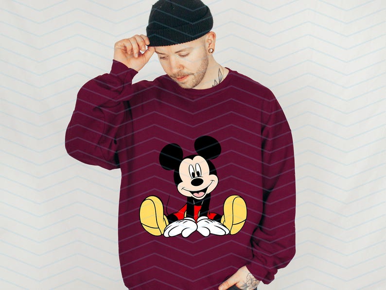 May include: A maroon sweatshirt featuring a cartoon image of Mickey Mouse sitting down. Mickey Mouse is wearing red shorts and yellow shoes.