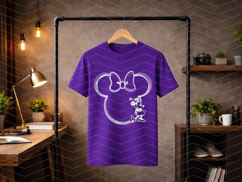 Puede incluir: Una camiseta morada con un contorno blanco de la cabeza y el lazo de Minnie Mouse, y una ilustraci&oacute;n detallada de Minnie Mouse. El dise&ntilde;o est&aacute; centrado en la camiseta.