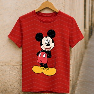 May include: A bright red short-sleeved t-shirt featuring a centered graphic of Mickey Mouse. The character is depicted with his signature black ears, white face, red shorts, and large yellow shoes, standing with hands on his hips.