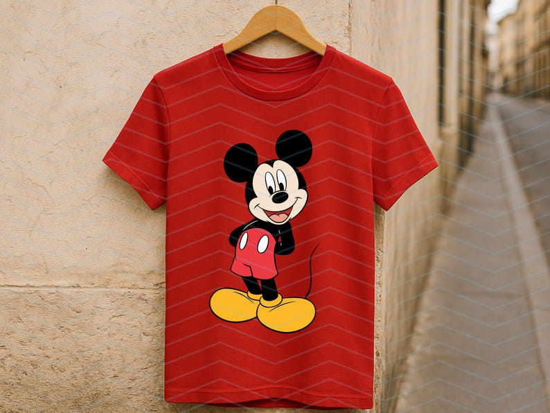 May include: A bright red short-sleeved t-shirt featuring a centered graphic of Mickey Mouse. The character is depicted with his signature black ears, white face, red shorts, and large yellow shoes, standing with hands on his hips.