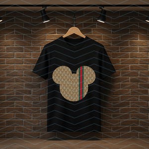 Puede incluir: Una camiseta negra de manga corta con un gr&aacute;fico central en forma de cabeza de rat&oacute;n. La silueta est&aacute; rellena con un patr&oacute;n repetitivo en tonos beige y marr&oacute;n e incluye una franja vertical de color rojo y verde en el lado derecho.