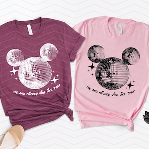 Puede incluir: Dos camisetas con un dise&ntilde;o de Mickey Mouse de bola de discoteca en blanco y negro. La camiseta granate dice "Me and Mickey vibe like that" y la camiseta rosa dice "Me and Mickey vibe like that".