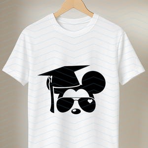 May include: White t-shirt featuring a black graphic of a mouse head wearing a graduation cap and sunglasses with a heart detail. The design is centered on the shirt, which hangs on a wooden hanger against a white and light blue chevron pattern.