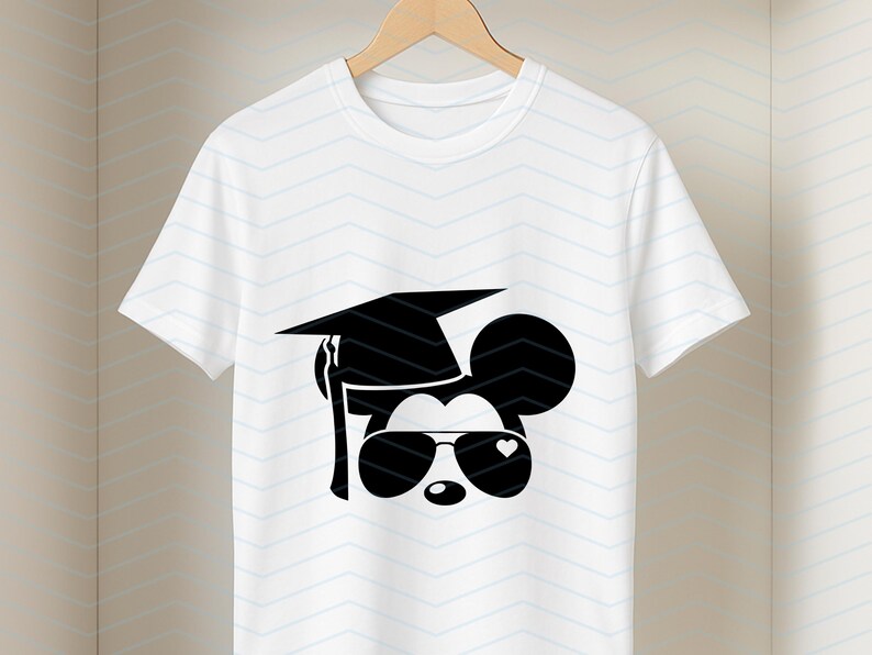 May include: White t-shirt featuring a black graphic of a mouse head wearing a graduation cap and sunglasses with a heart detail. The design is centered on the shirt, which hangs on a wooden hanger against a white and light blue chevron pattern.