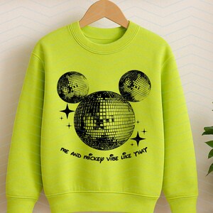 Puede incluir: Una sudadera verde brillante con un gr&aacute;fico negro de una cabeza de Mickey Mouse hecha de bolas de discoteca. El texto "Me and Mickey vibe like that" est&aacute; impreso debajo del gr&aacute;fico.