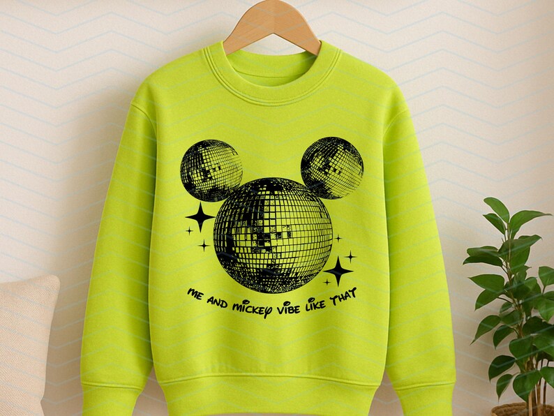 Puede incluir: Una sudadera verde brillante con un gr&aacute;fico negro de una cabeza de Mickey Mouse hecha de bolas de discoteca. El texto "Me and Mickey vibe like that" est&aacute; impreso debajo del gr&aacute;fico.
