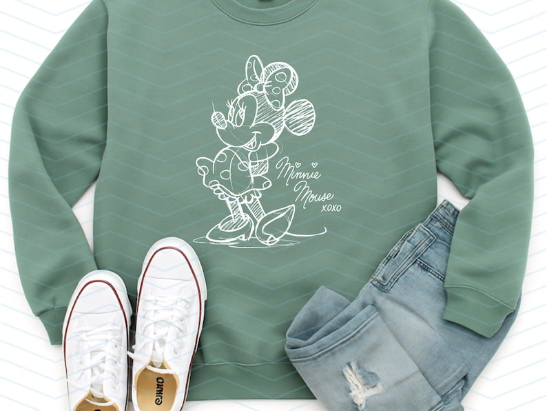May include: Sage green sweatshirt with a white sketch of Minnie Mouse, paired with light wash denim jeans and white sneakers. The sweatshirt features the text "Minnie Mouse xoxo".