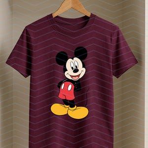 May include: A maroon short-sleeved t-shirt featuring a centered graphic of Mickey Mouse. The character is depicted with his signature black ears, red shorts, and large yellow shoes, standing with a cheerful expression on his face.