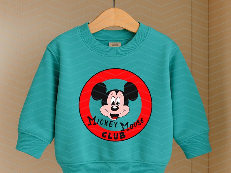May include: A teal long-sleeve sweatshirt featuring a subtle chevron pattern and a central graphic of Mickey Mouse inside a red circle. The text "MICKEY MOUSE CLUB" is printed in black lettering below the character's face on the front of the garment.