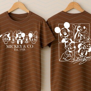 May include: A brown short-sleeved t-shirt featuring white graphic prints. The front displays five cartoon character faces with the text MICKEY & CO Est. 1928. The back shows a four-panel grid of characters with the text MICKEY MOUSE.