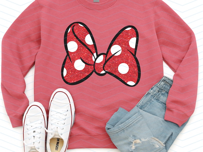 Puede incluir: Una sudadera roja con un gran lazo brillante con lunares blancos y un contorno negro. La imagen tambi&eacute;n muestra un par de zapatillas blancas y unos vaqueros azules.