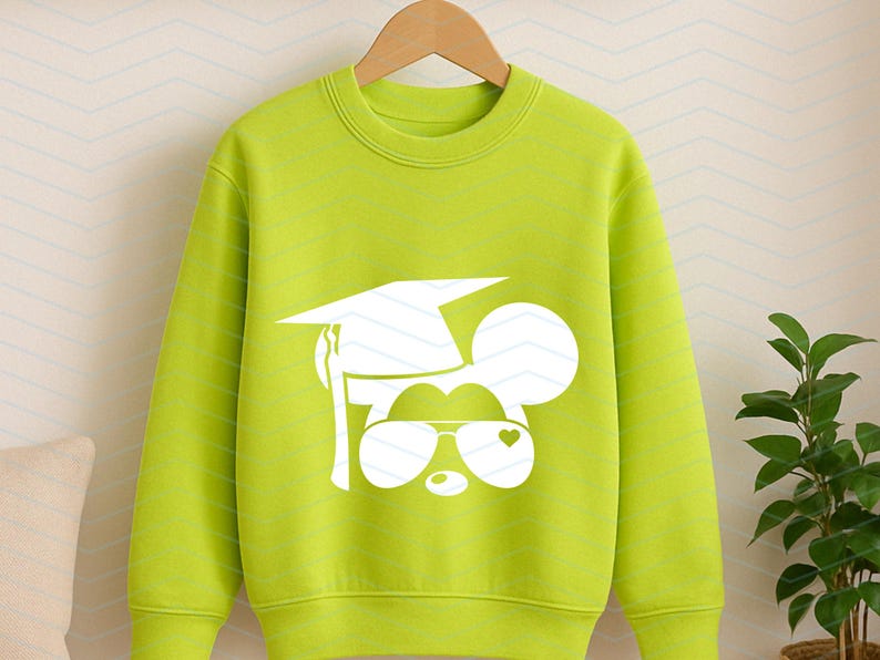 May include: Lime green sweatshirt with a white graphic of a mouse wearing a graduation cap and sunglasses with a heart. The sweatshirt is hanging on a wooden hanger.