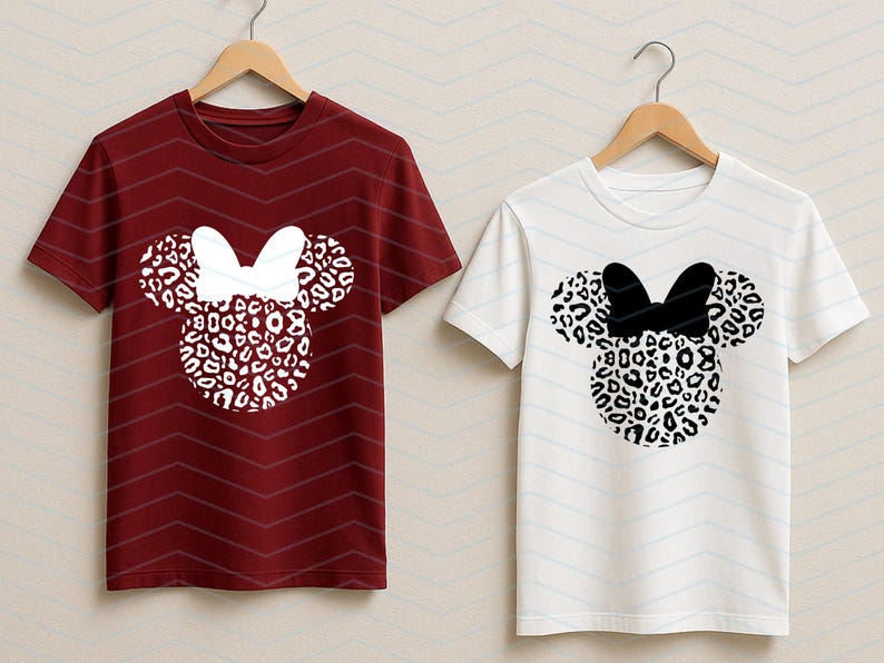 May include: Two short-sleeved t-shirts, one burgundy and one white, each featuring a Minnie Mouse design. The design includes a leopard print head and ears with a bow. The burgundy shirt has a white bow, while the white shirt has a black bow.