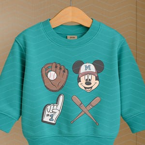 May include: A teal blue sweatshirt with a baseball glove, baseball, and Mickey Mouse graphic. The Mickey Mouse graphic has a baseball cap with the letter "M" on it. The text "#1" is on the graphic of a raised finger.