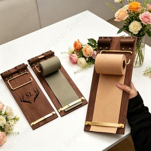 May include: Three wooden memo boards with brass detailing. The boards have a dark wood finish and feature a roll of paper. One board has the initials "SL" and a deer antler design. The boards are displayed on a white surface.