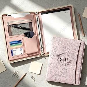 May include: A light pink zippered portfolio organizer featuring an embossed floral pattern on the cover with the letters GH inside a circular wreath. The interior includes a memo pad, a metal ring binder, card slots, a phone pocket, and a mesh pouch.
