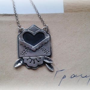 Puede incluir: Collar de plata con un colgante en forma de coraz&oacute;n que parece un sobre. El sobre tiene un dise&ntilde;o decorativo y est&aacute; abierto para revelar el coraz&oacute;n.