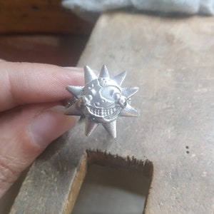 Peut inclure: Une bague en argent avec un motif en forme d'étoile. Le centre de l'étoile présente un visage souriant avec un large sourire aux dents.