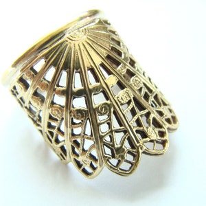 May include: A gold-colored metal ring with a decorative, openwork design. The ring is shaped like a fan and has a scalloped edge.