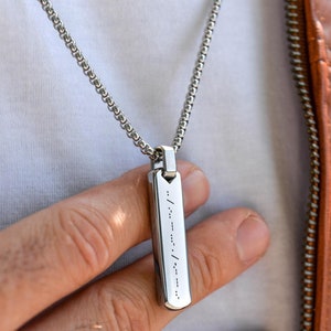 May include: A silver chain necklace with a silver pendant. The pendant is rectangular and has a pattern of dots and dashes on it.