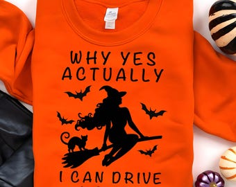 May include: An orange crewneck sweatshirt featuring a black graphic of a witch riding a broomstick with a cat and bats. The text reads: WHY YES ACTUALLY I CAN DRIVE A STICK. The design is centered on the front of the garment, which has a white tag.