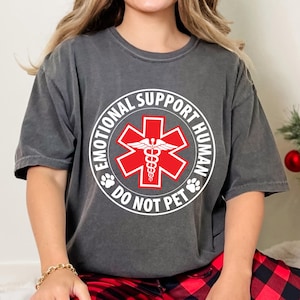 May include: A gray t-shirt with a white circle graphic that says "Emotional Support Human Do Not Pet". The graphic also features a red medical symbol with a snake and wings.