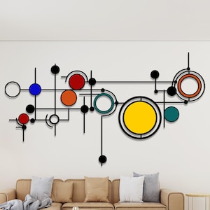 Op de afbeelding: Abstracte wandkunst met een zwart lineair ontwerp en kleurrijke cirkels in rood, blauw, oranje, geel en teal. Het kunstwerk is gemonteerd op een witte muur boven een bruine bank, wat een moderne woonkameresthetiek creëert.