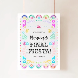 May include: A white sign with colorful floral and geometric designs. The text reads "Welcome to Monica's FINAL ¡FIESTA!" with "Cabo • Mexico" below. The sign is suspended by a thin string.