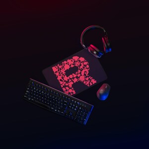 Puede incluir: Un teclado de ordenador negro, un ratón inalámbrico y unos auriculares negros dispuestos alrededor de una alfombrilla rectangular. La alfombrilla muestra una letra R grande compuesta por pequeñas siluetas rosas de criaturas.