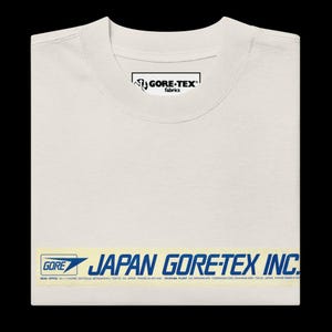 Puede incluir: Una camiseta blanca con una etiqueta azul y amarilla que dice "GORE JAPAN GORE-TEX INC." e incluye la información de contacto de la oficina central y la planta de la empresa.