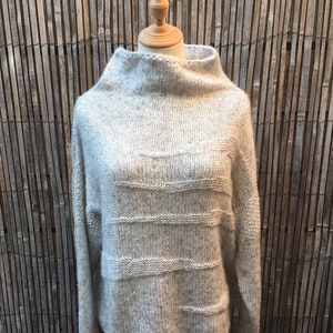 May include: A light gray knitted sweater with a high neck and horizontal stripes. The sweater is on a mannequin against a bamboo background.