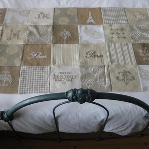 Puede incluir: Un edredón blanco con un diseño de patchwork que presenta varias palabras y símbolos bordados, incluyendo "Fleur", "Paris", "anno 2010", "merci bonjour mon ami" y "Co Aa Is DoF".