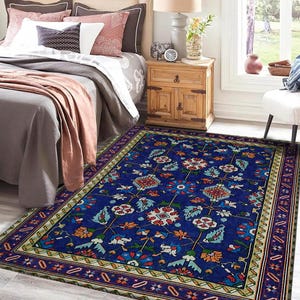 May include: A blue rug with a floral pattern and a multi-coloured border. The rug is in a bedroom setting with a bed and bedside table.