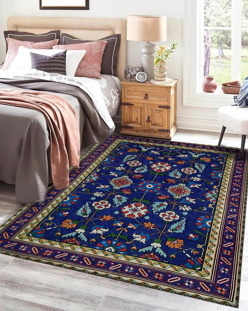 May include: A blue rug with a floral pattern and a multi-coloured border. The rug is in a bedroom setting with a bed and bedside table.