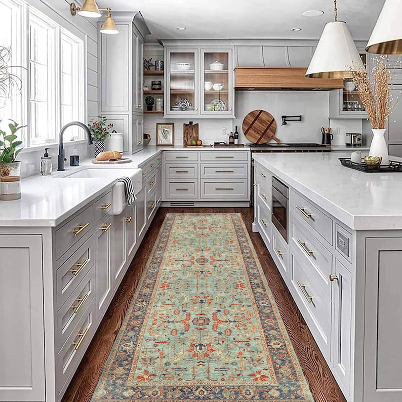 May include: A light grey kitchen with white worktops and cabinets. A patterned rug runs down the centre of the kitchen floor.