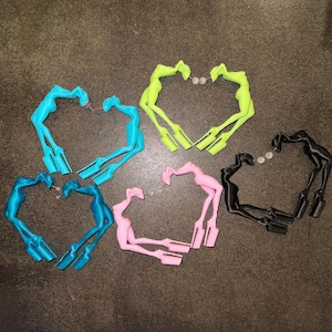 Könnte beinhalten: Fünf Paar Creolen in Form von menschlichen Figuren mit Plateauschuhen. Die Ohrringe sind in leuchtendem Blau, Neongrün, Dunkelblau, Hellrosa und Schwarz erhältlich und verfügen jeweils über einen kleinen Stecker zur Befestigung.