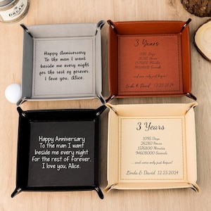 Puede incluir: Cuatro bandejas cuadradas de cuero en gris, marrón, negro y crema. Cada bandeja tiene un mensaje diferente, incluyendo "Happy Anniversary" y "3 Years" con una fecha. Las bandejas están diseñadas para guardar objetos pequeños.