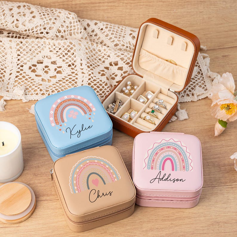 May include: Three small, square, personalized jewelry boxes with rainbow designs. The boxes are blue, pink, and brown. Each box has a name on it: Kylie, Addison, and Chris.