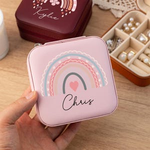 May include: Pink jewelry box with a rainbow and heart design. The box has the name "Chris" written on it.