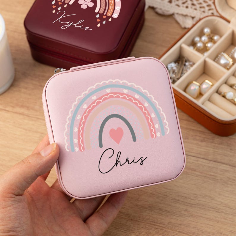 May include: Pink jewelry box with a rainbow and heart design. The box has the name "Chris" written on it.