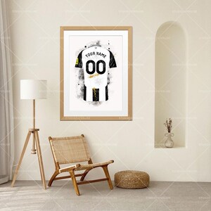 May include: Framed art print of a soccer jersey in black and white with the number "00" and the text "YOUR NAME". The jersey design is a watercolor style with black paint splatters.