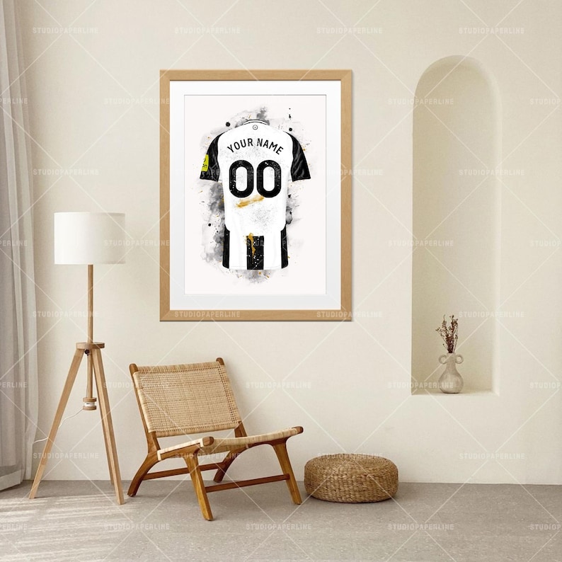 May include: Framed art print of a soccer jersey in black and white with the number "00" and the text "YOUR NAME". The jersey design is a watercolor style with black paint splatters.