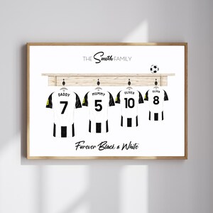 May include: A framed print featuring four black and white soccer jerseys hanging on a wooden rack. Each jersey has a name and number: Daddy 7, Mummy 5, Oliver 10, and Olivia 8. The text "The Smith Family" and "Forever Black & White" are also displayed.