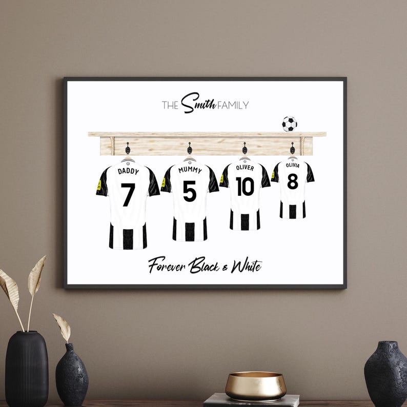 May include: A framed print featuring four soccer jerseys hanging on a wooden rack. Each jersey is white with black stripes and a number. The names "Daddy," "Mummy," "Oliver," and "Olivia" are above the jerseys. The text "Forever Black & White" is below.
